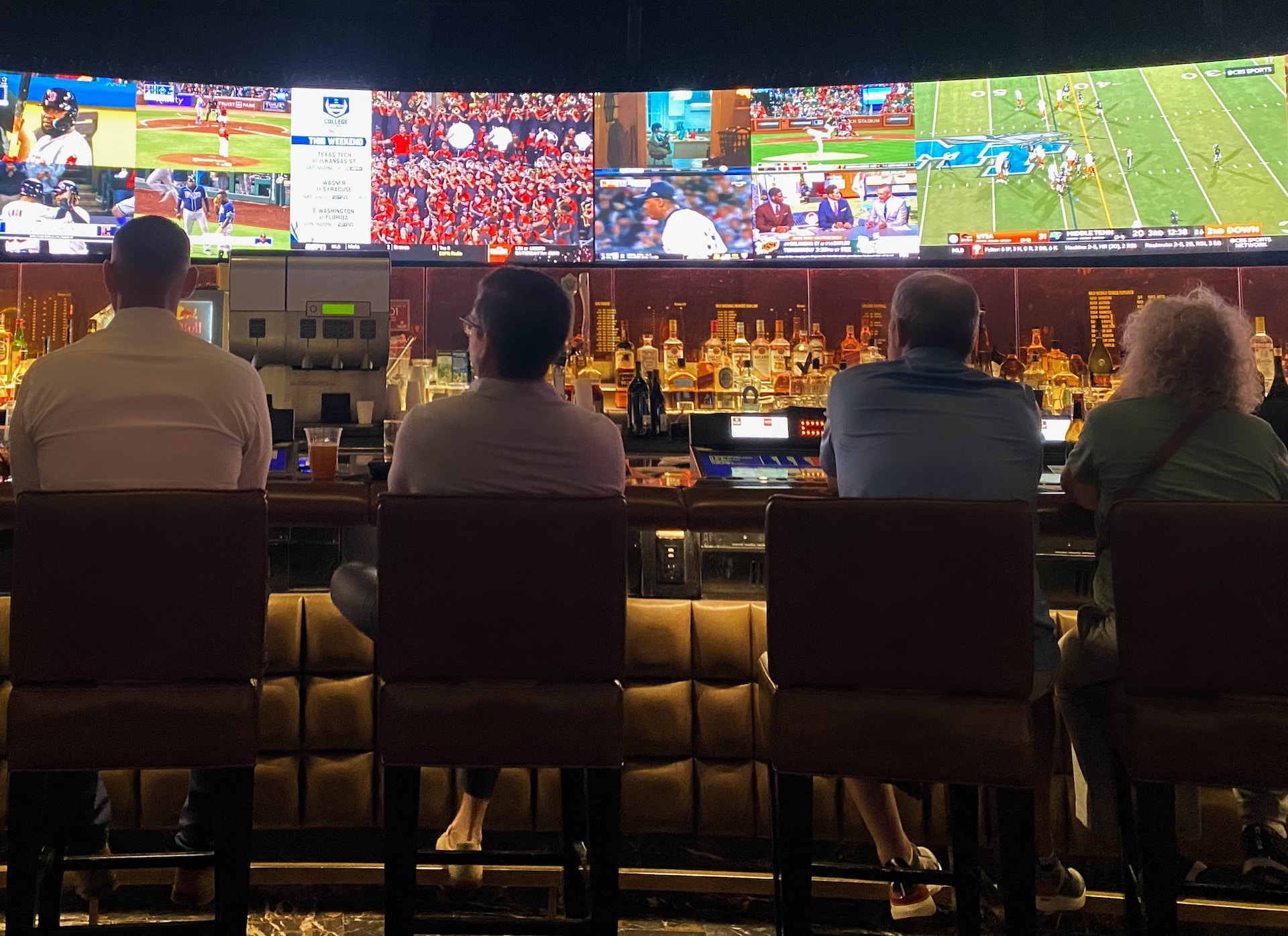 A group of people sitting at a bar watching television. A group of people sitting at a bar watching television.